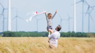 Isä ja lapsi pellolla, jossa tuulivoimaloita