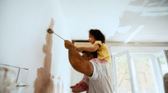 Lapsi miehen hartioilla maalaa kodin sisäseinää