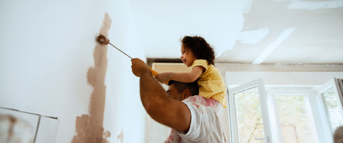 Lapsi miehen hartioilla maalaa kodin sisäseinää