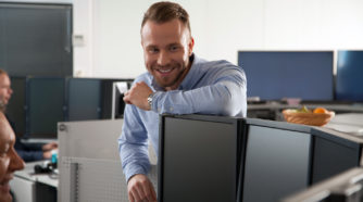 Hymyilevä nuori mies seisoo ja nojaa toimistossa pöytään