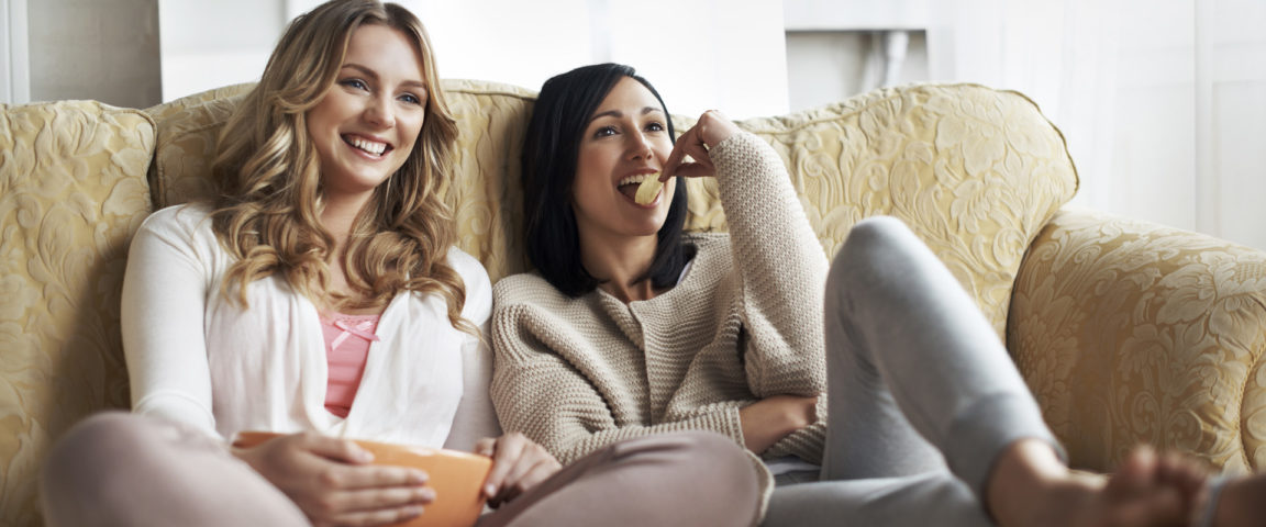 Naiset istuvat sohvalla syömässä sipsejä
