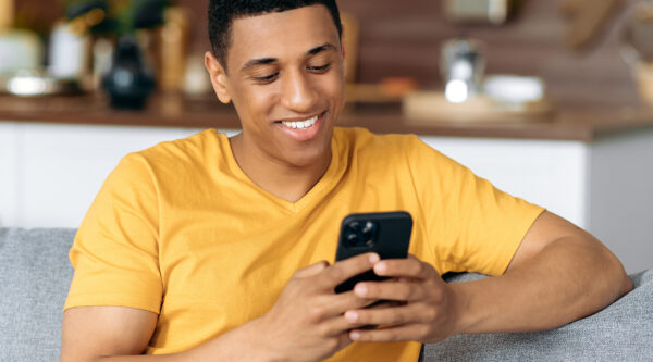 Henkilö istuu sohvalla ja hoitaa asioitaan puhelimellaan.