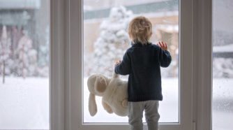 Lapsi ikkunassa katsoo ulos pehmolelu kädessä