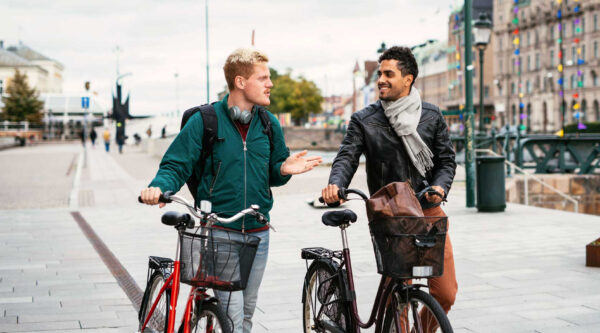 Kaksi nuorta miestä taluttaa polkupyöriä kaupungilla